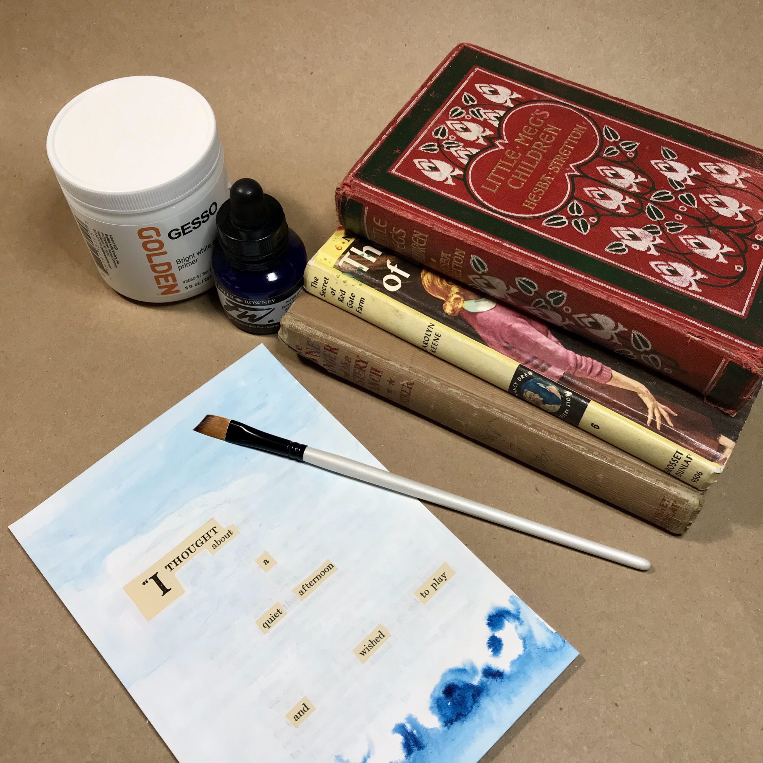 A vintage book page painted to hide most of the text, a stack of books, paintbrush, art supplies
